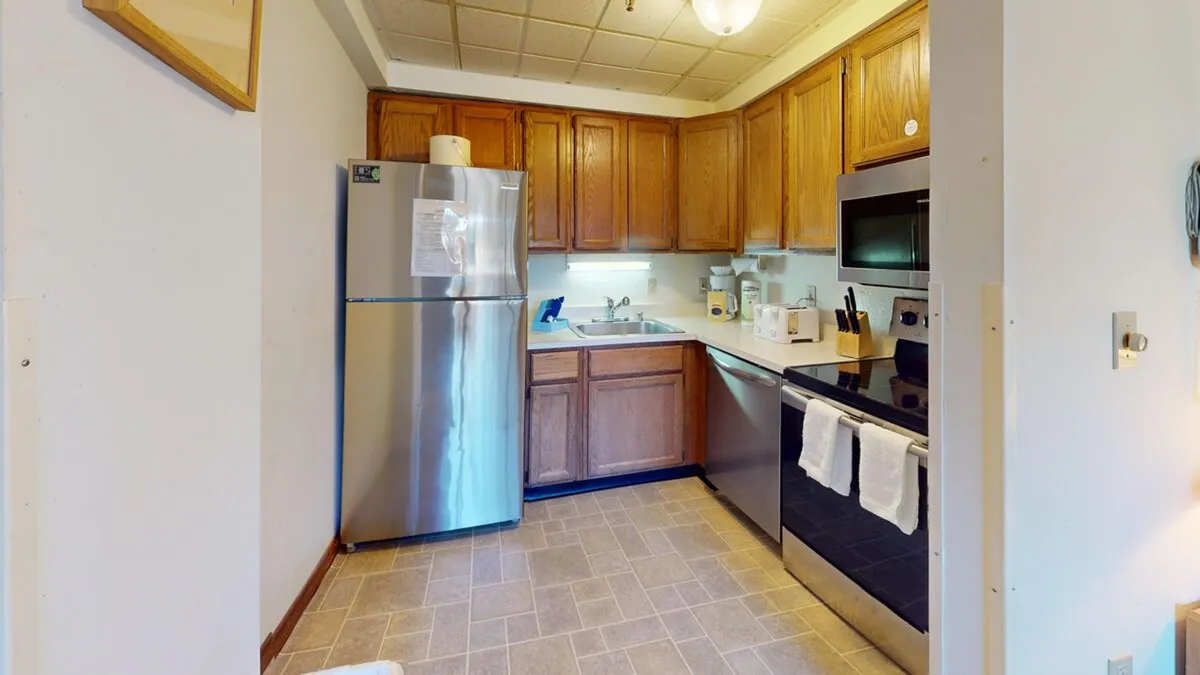 A homey kitchen scene featuring a stainless steel refrigerator, dark cabinetry, a black stove and microwave, and a sink beneath a window. The layout suggests ample space for meal preparation and socializing, with natural light brightening the area.