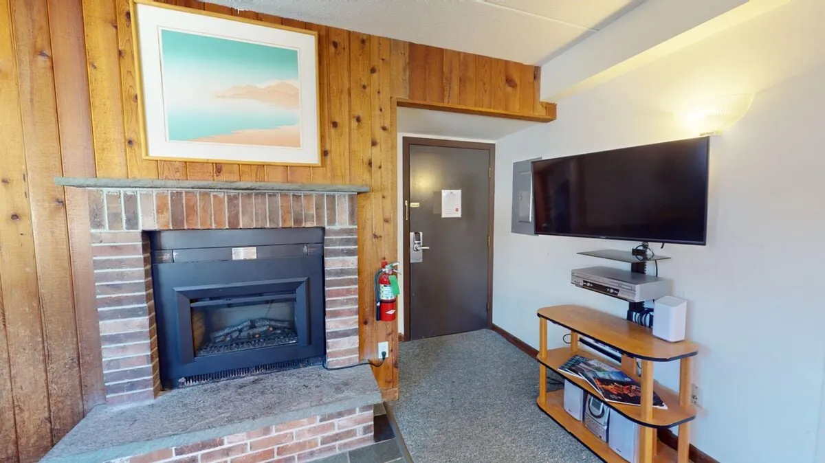 A comfortable living room with wood paneling, a plush sofa, framed artwork, and a fireplace, bathed in warm, inviting lighting. The overall atmosphere is designed for cozy evenings, with spaces for watching TV, relaxing, and enjoying artful touches.