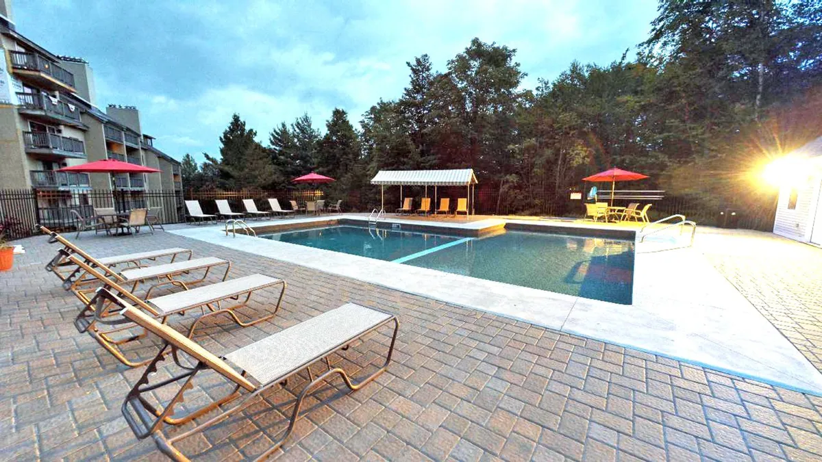 An exterior view of the resort's swimming pool area, with lounge chairs, cabana, and umbrellas arranged for guest comfort. The inviting poolside setting emphasizes leisure and relaxation in a social, outdoor environment.