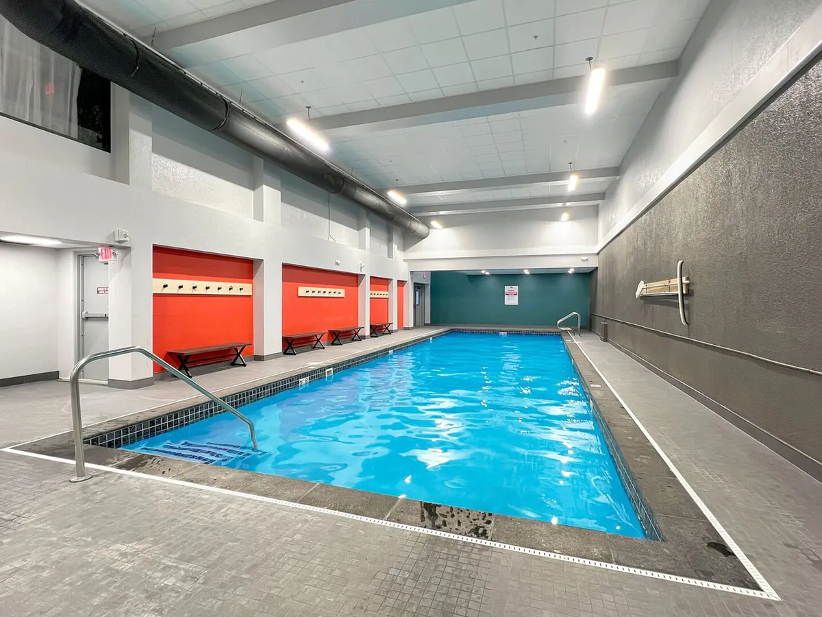 A bright, contemporary indoor swimming pool with sparkling blue water, accented by red and gray walls. The pool is inviting, spacious, and well-lit, making it ideal for year-round relaxation or exercise.