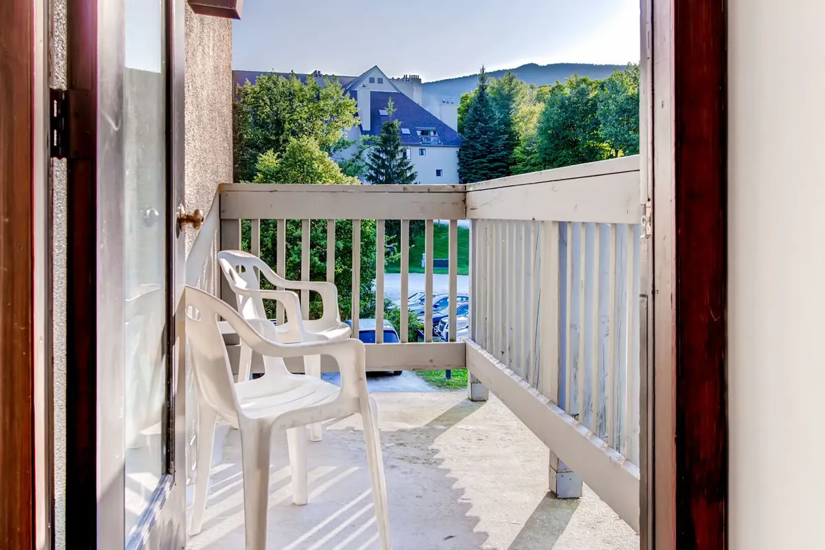 This inviting exterior image shows a tranquil balcony with chairs, offering scenic views of surrounding trees and nearby buildings. The setting evokes relaxation and opportunities for families to gather outdoors, take in nature, or enjoy a cup of coffee after an active day exploring Killington.