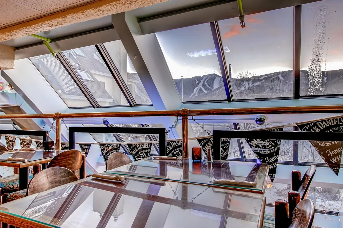 A cozy interior dining space with large windows framing scenic mountain views, several dining tables, and decorative banners. The environment is comfortable and relaxed, suited for family meals or enjoying the on-site restaurant's offerings after a day of adventure.