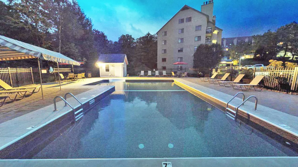 An exterior shot of the swimming pool area, featuring a serene pool surrounded by lounge chairs, a canopy, and lush trees, with the building visible in the background. The scene feels calm, inviting, and perfect for family swims or social gatherings under the stars.