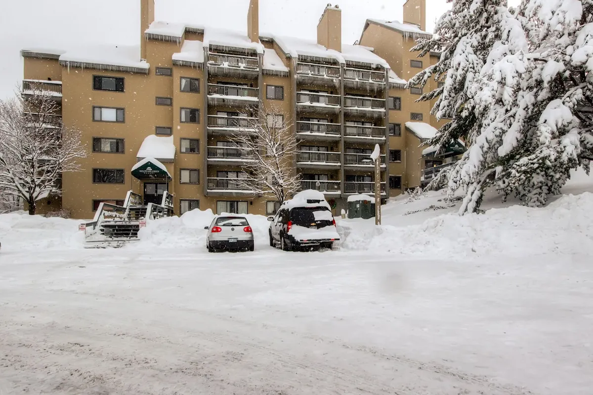 A snow-covered building surrounded by parked cars and trees, capturing the essence of winter at the resort. The image exudes a tranquil, wintry atmosphere and hints at ski-in/ski-out convenience, with easy access to the slopes just a short walk away.