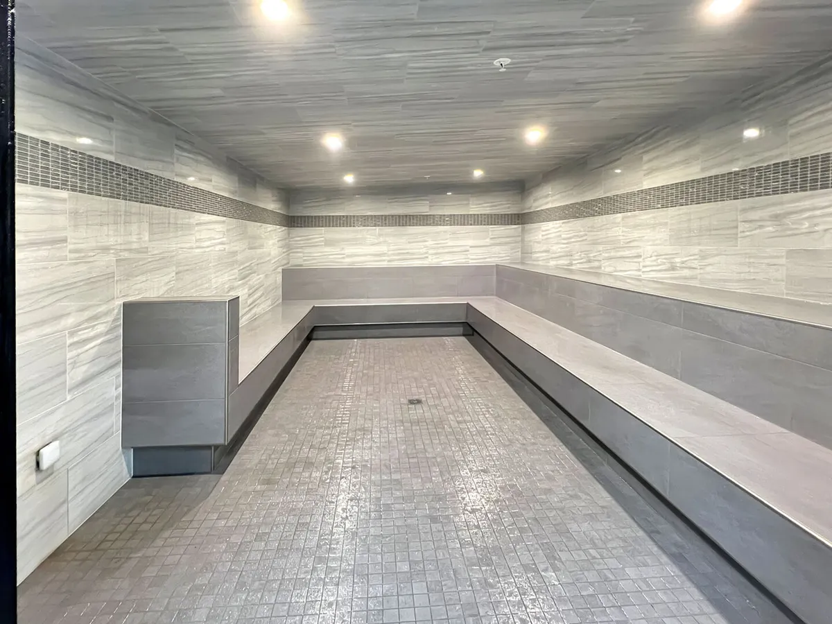 A tranquil interior space with smooth gray tile walls, bench seating, and even lighting, evoking the calm environment of a steam room or spa relaxation area.